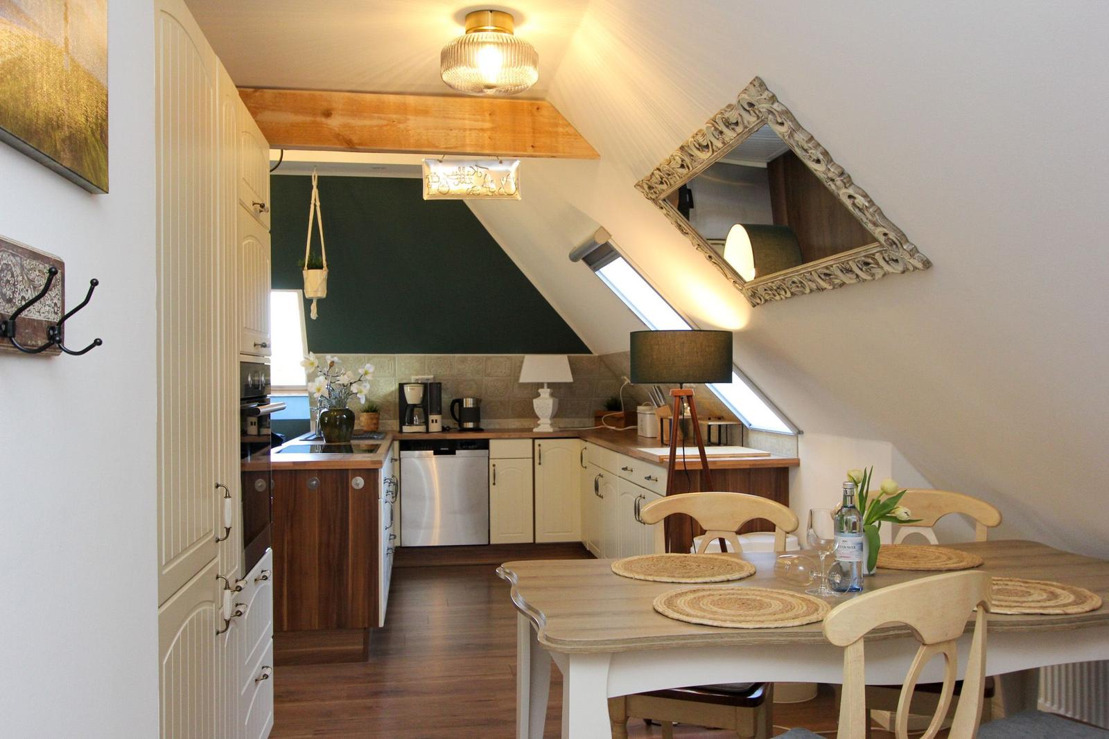 Küche mit Essbereich unter Dachschräge, Holztisch, Stühle, Spüle, Dunstabzug und Fenster.