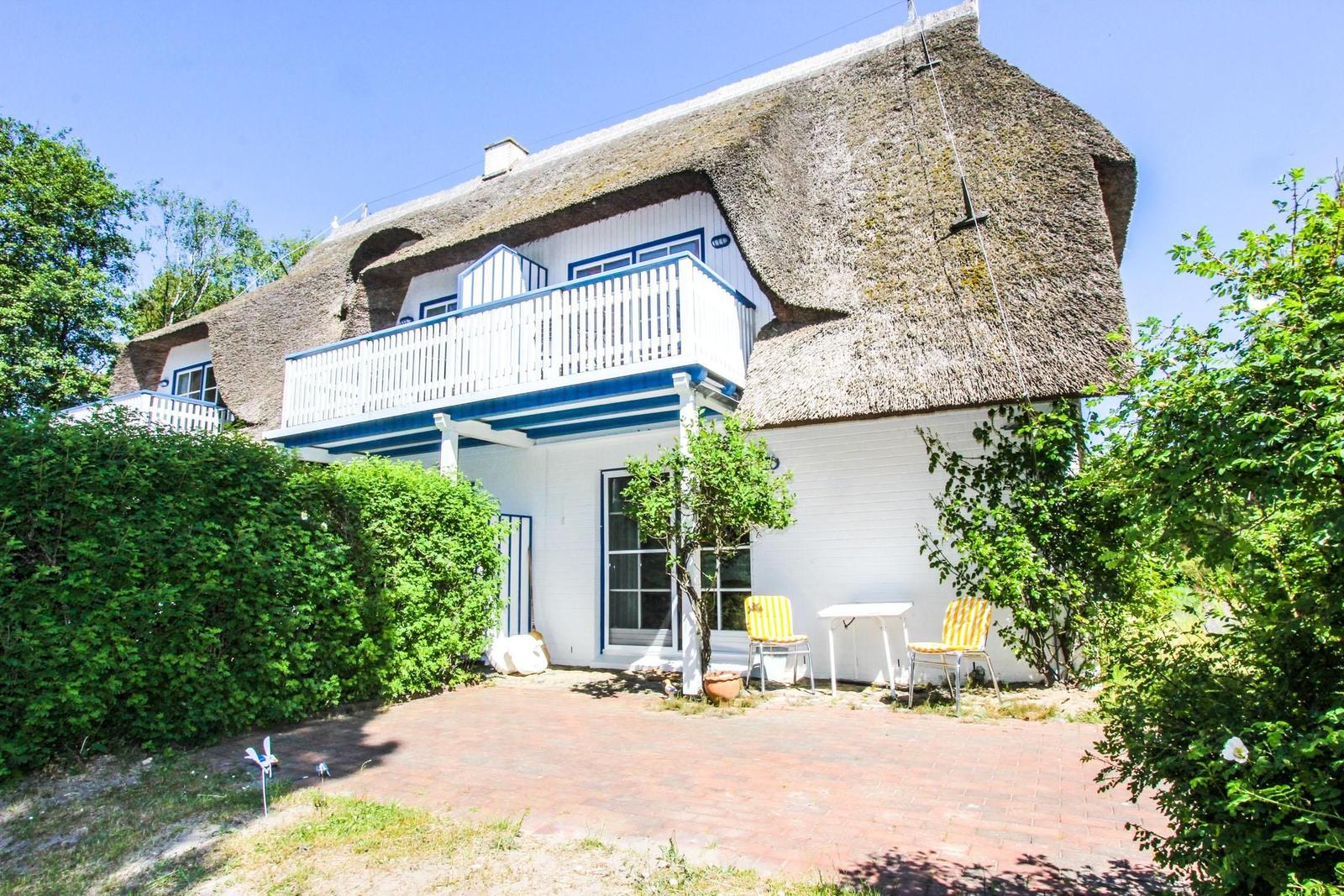Haus mit Strohdach, Balkon und Terrasse mit Stühlen und Tisch.
