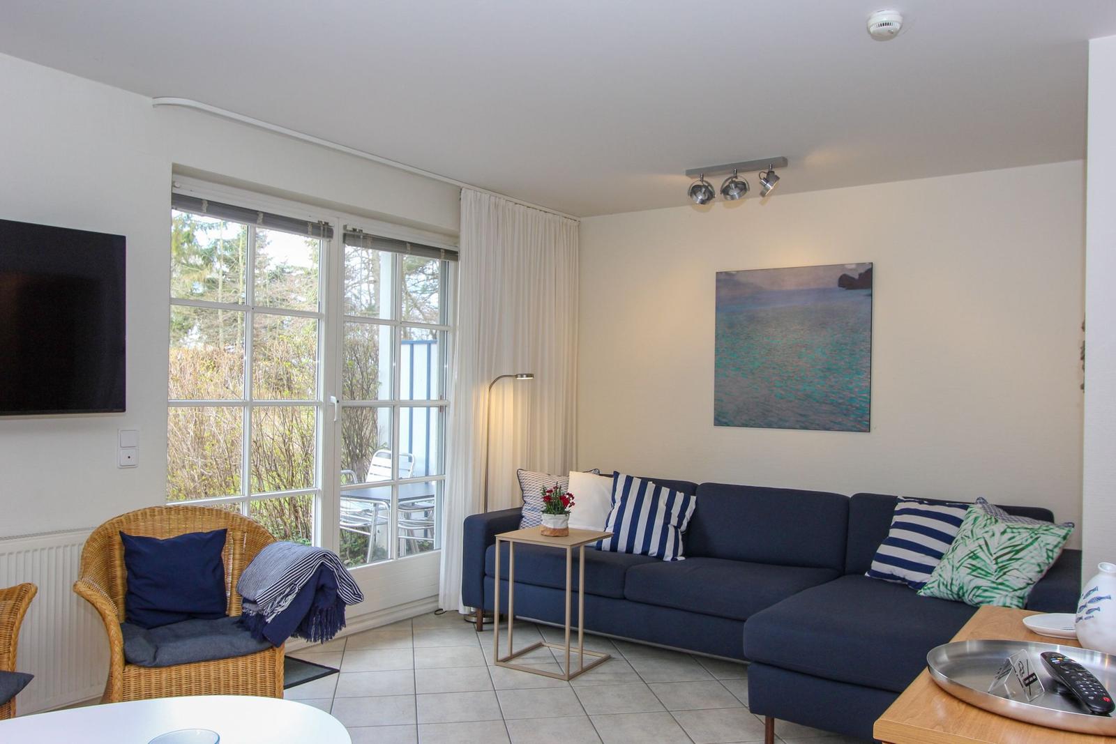 Wohnzimmer mit Sofa, Sessel und Fenster zur Terrasse.