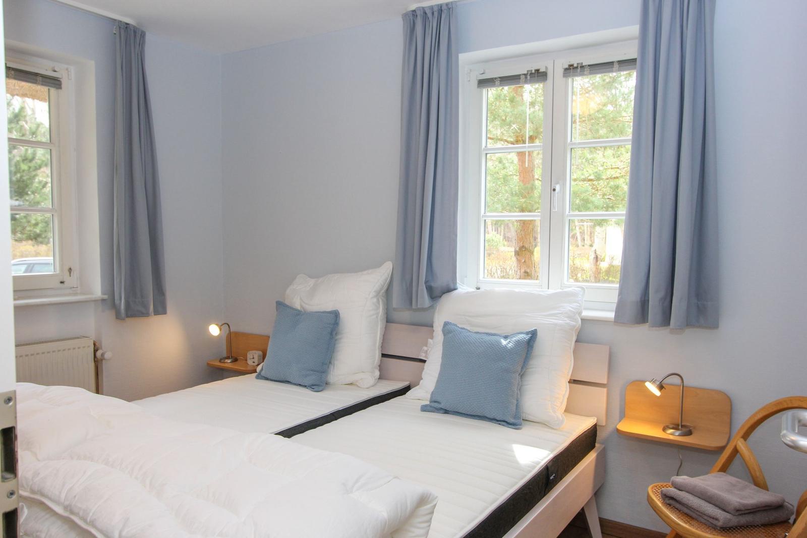 Zimmer mit Doppelbett, zwei Fenstern und Holzsideboards mit Lampen.