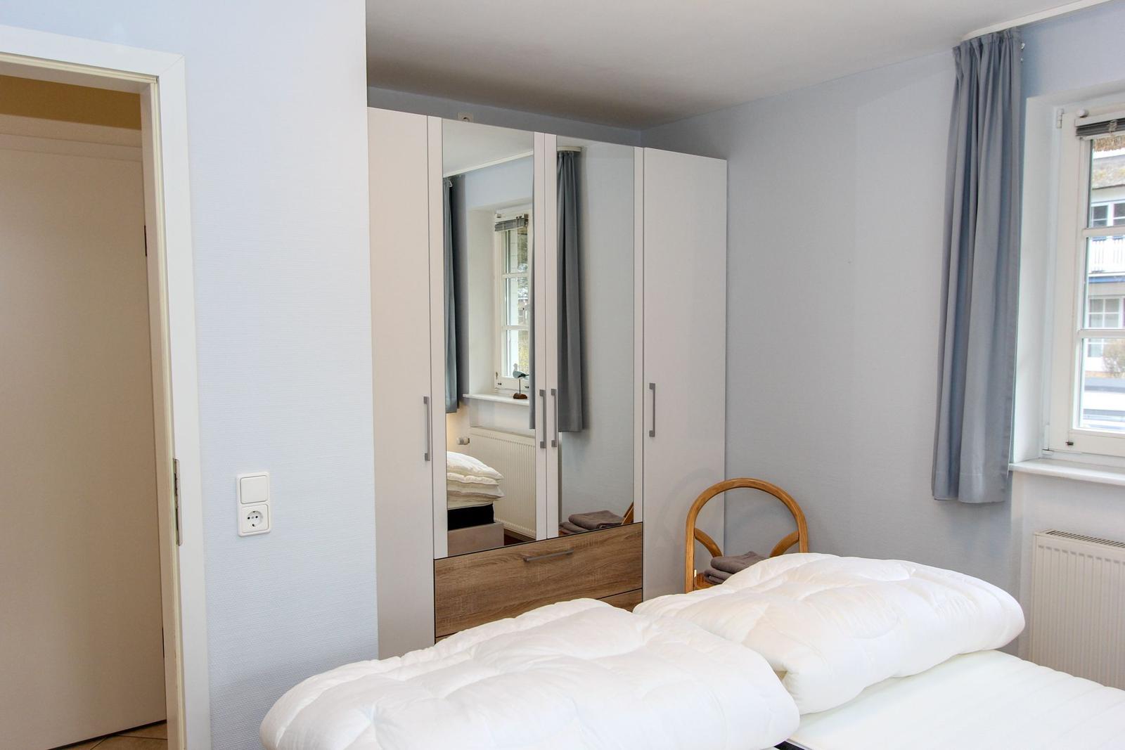 Schlafzimmer mit Bett, Kleiderschrank und Fenster mit Vorhängen.