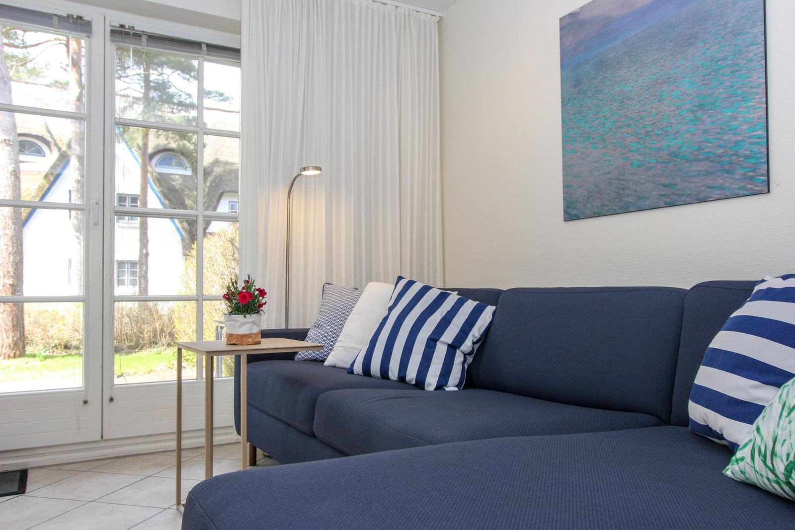 Ein Wohnzimmer mit blauem Sofa, Kissen und einer Glastür zum Garten.
