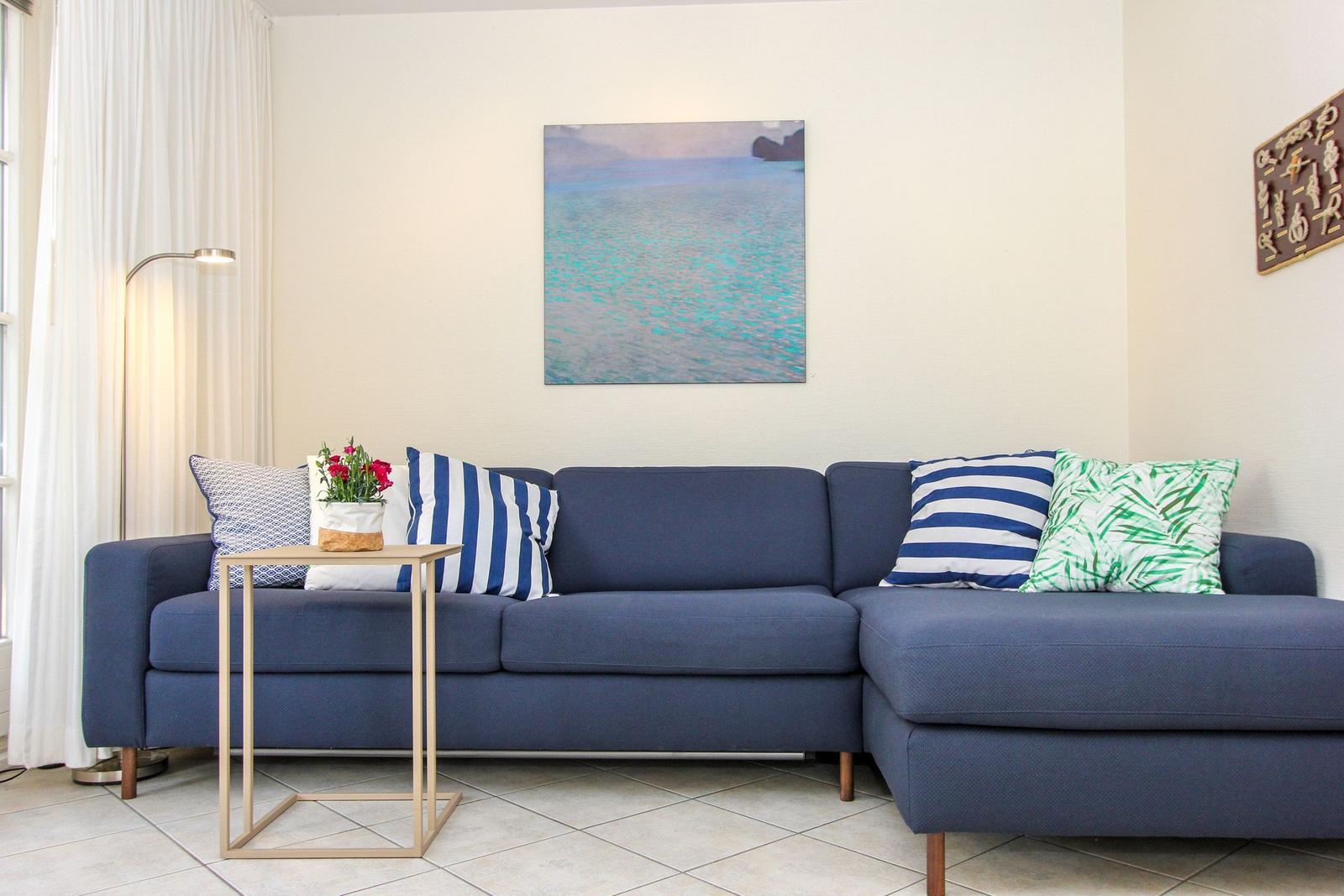 Ein blauer Sofa mit Kissen und einem Tisch vor einer Wand mit Bild.