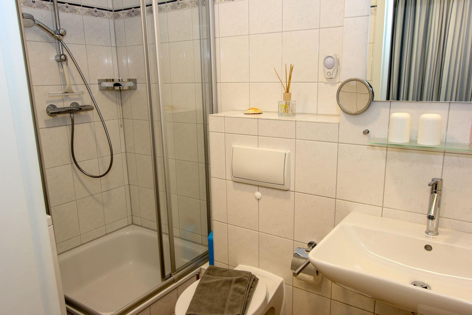 Badezimmer mit Dusche, Waschbecken und Toilette. Fliesenwand, Spiegel und Handtuch.