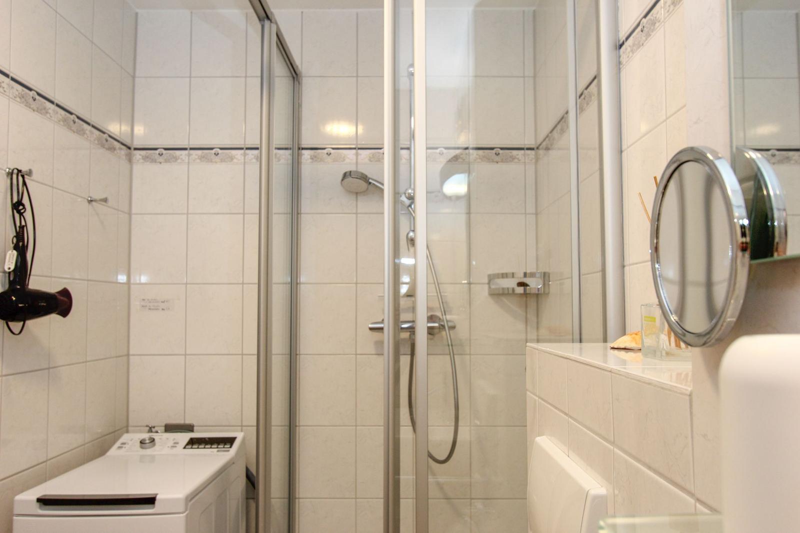 Badezimmer mit Dusche, Waschmaschine und runden Spiegel.