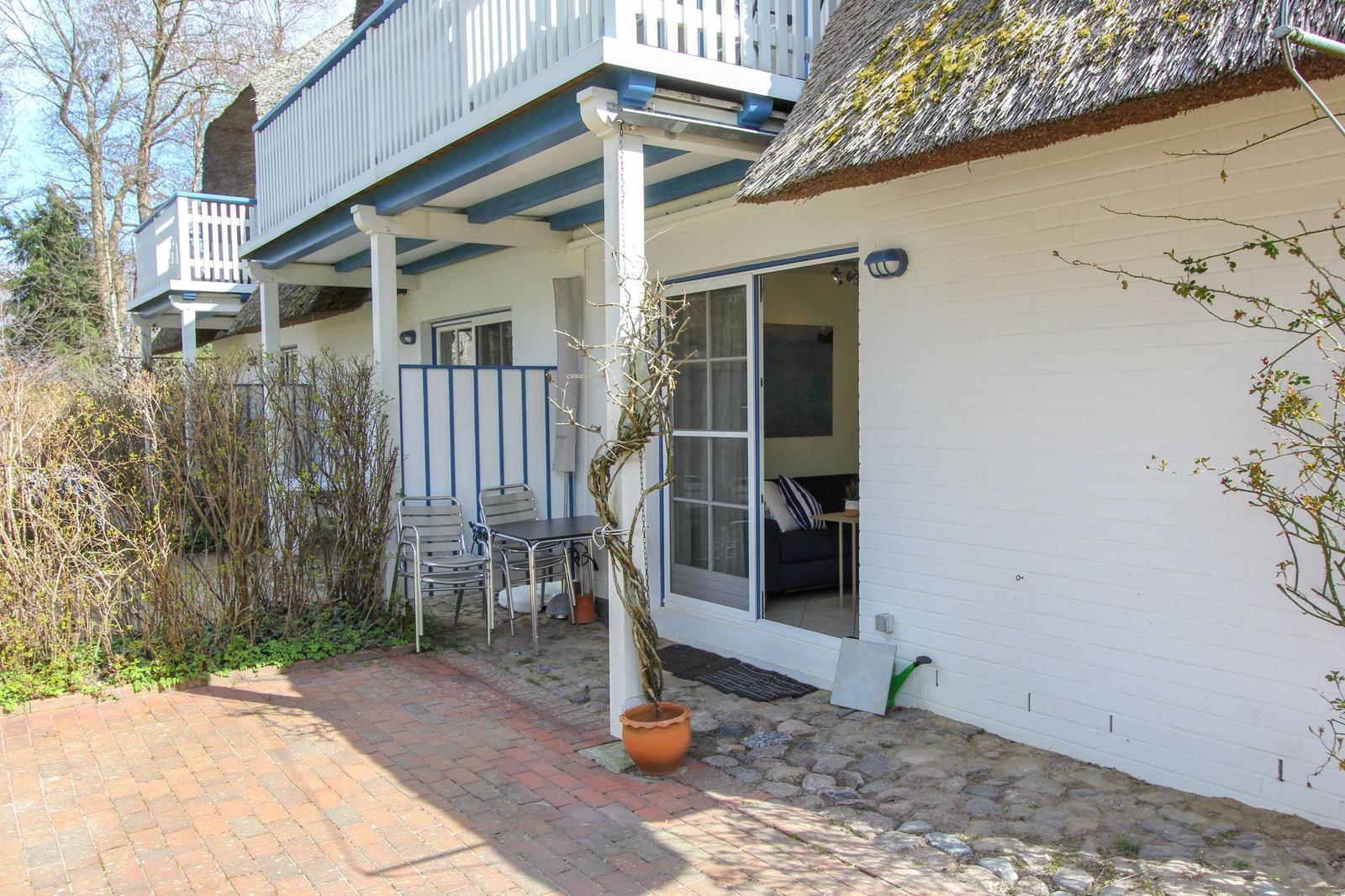 Wohnung mit Terrasse, Gartentisch und Schiebetür. Dach aus Stroh, weißer Putz, Pflanzen.