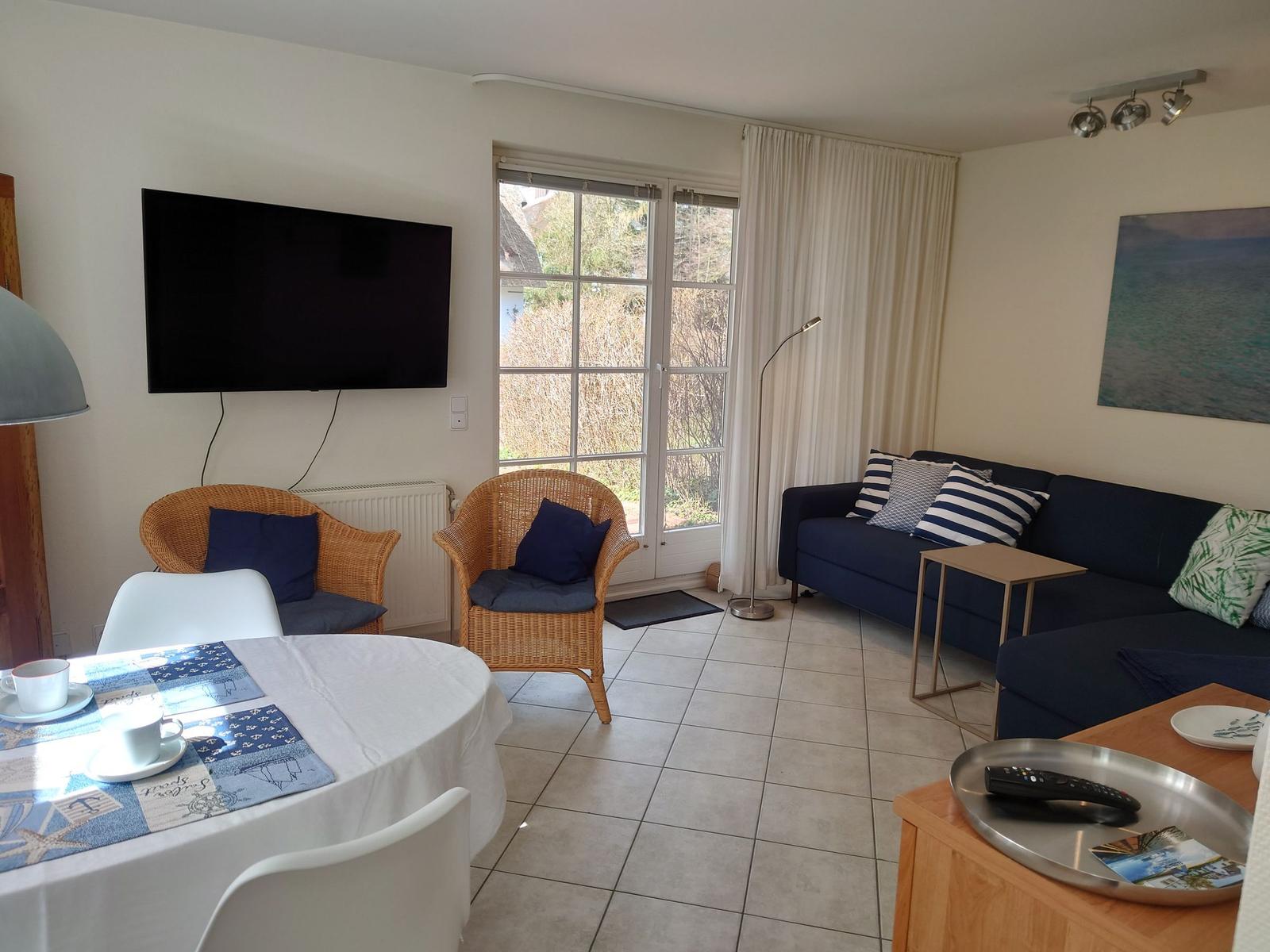 Wohnzimmer mit Sofa, Esstisch und TV. Fenster zur Außenseite.