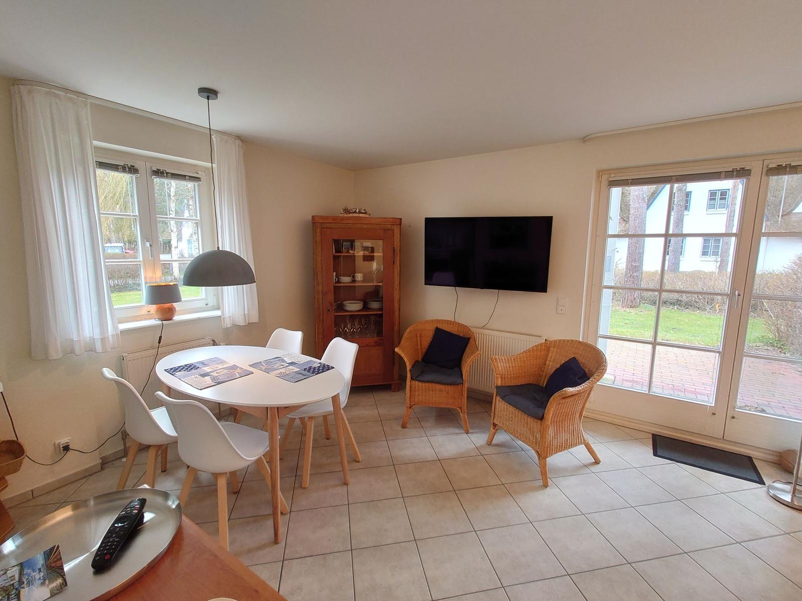 Essbereich mit Tisch und Stühlen, Fernseher und zwei Rattan-Stühle an der Wand.