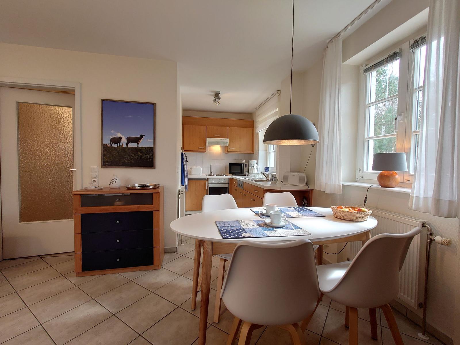 Esszimmer mit runder Tisch, vier Stühlen und Küchenbereich im Hintergrund.