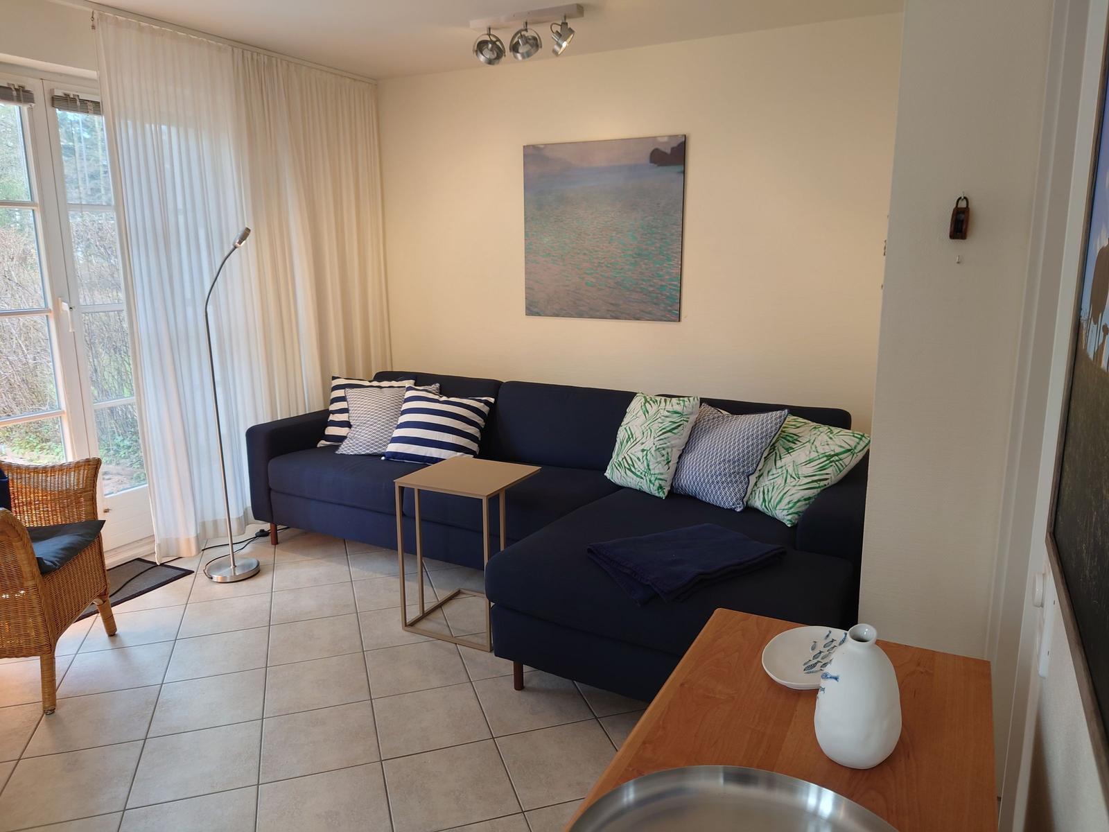 Ein Wohnzimmer mit blauem Sofa, Fenstern und Wandbild.