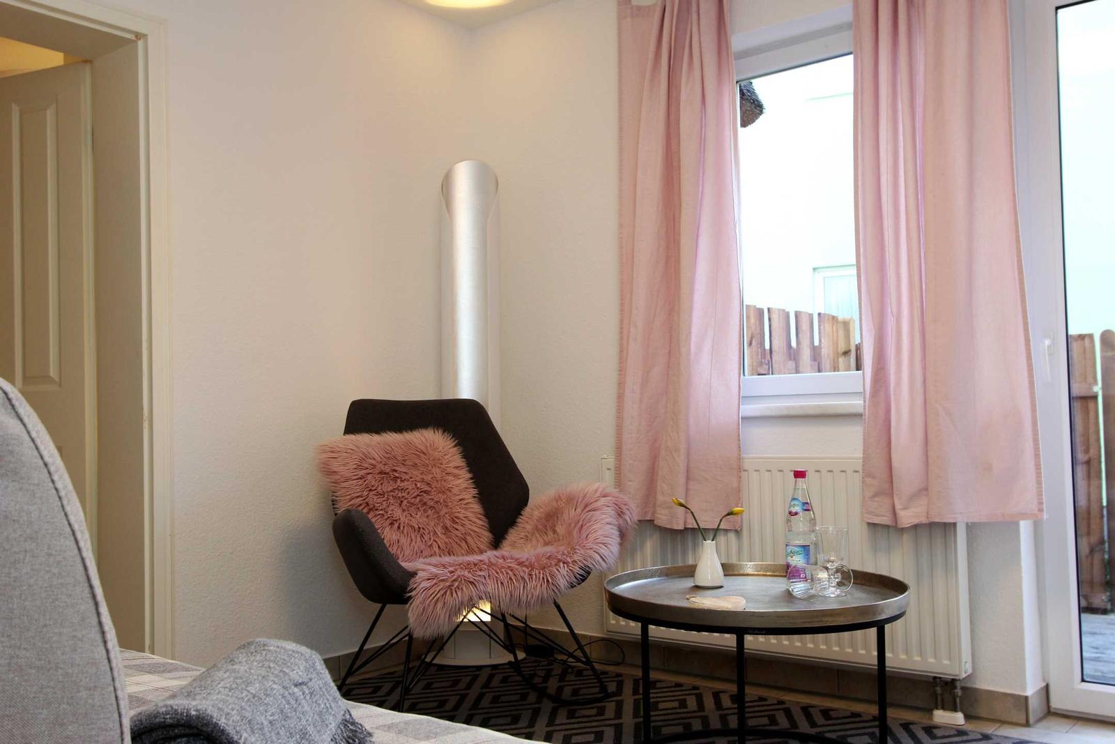 Ein Raum mit einem Stuhl, rosa Fell und einem Tisch vor einem Fenster mit rosa Vorhängen.
