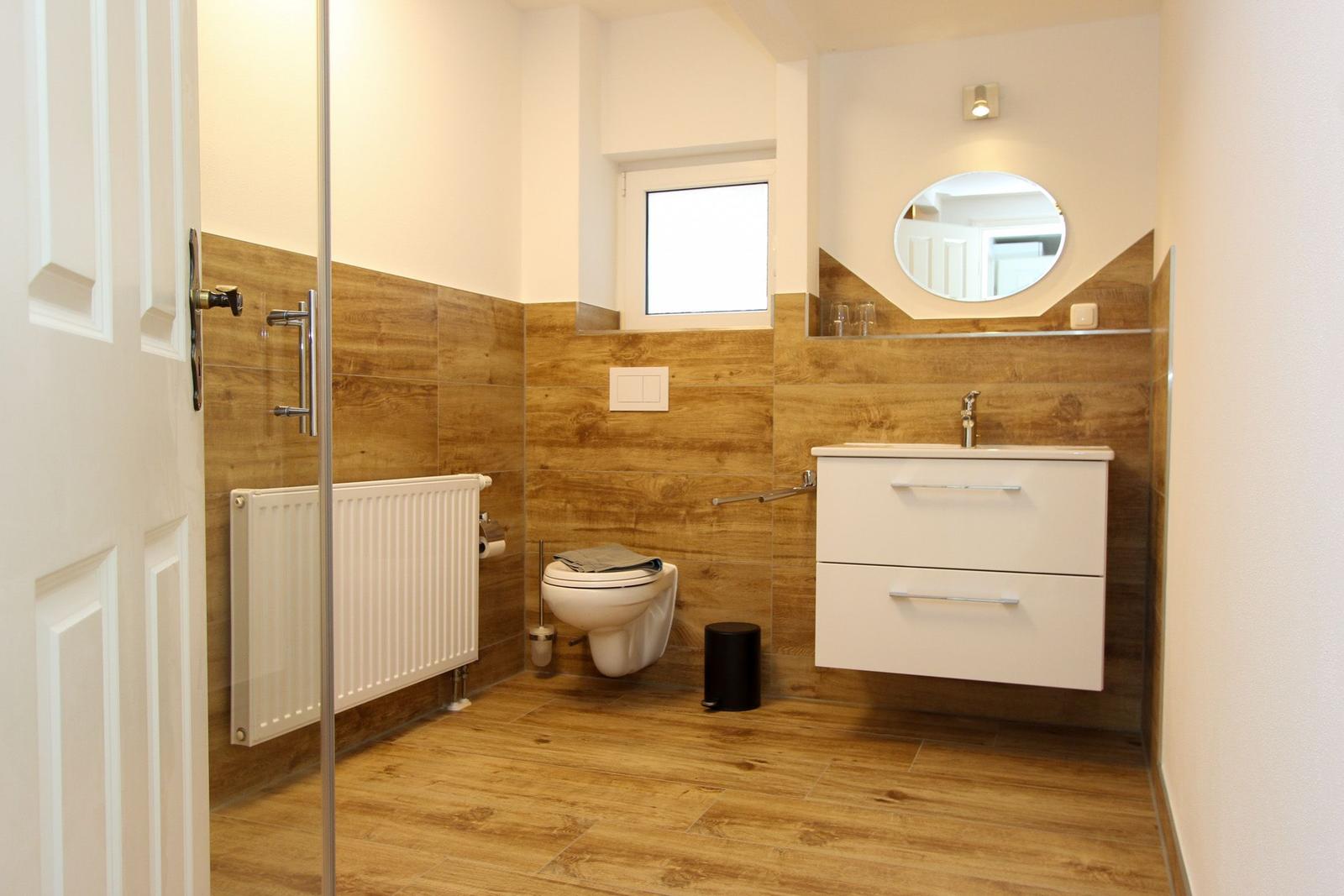 Badezimmer mit Holzoptik, Waschtisch, Toilette und Dusche mit Glaswand.