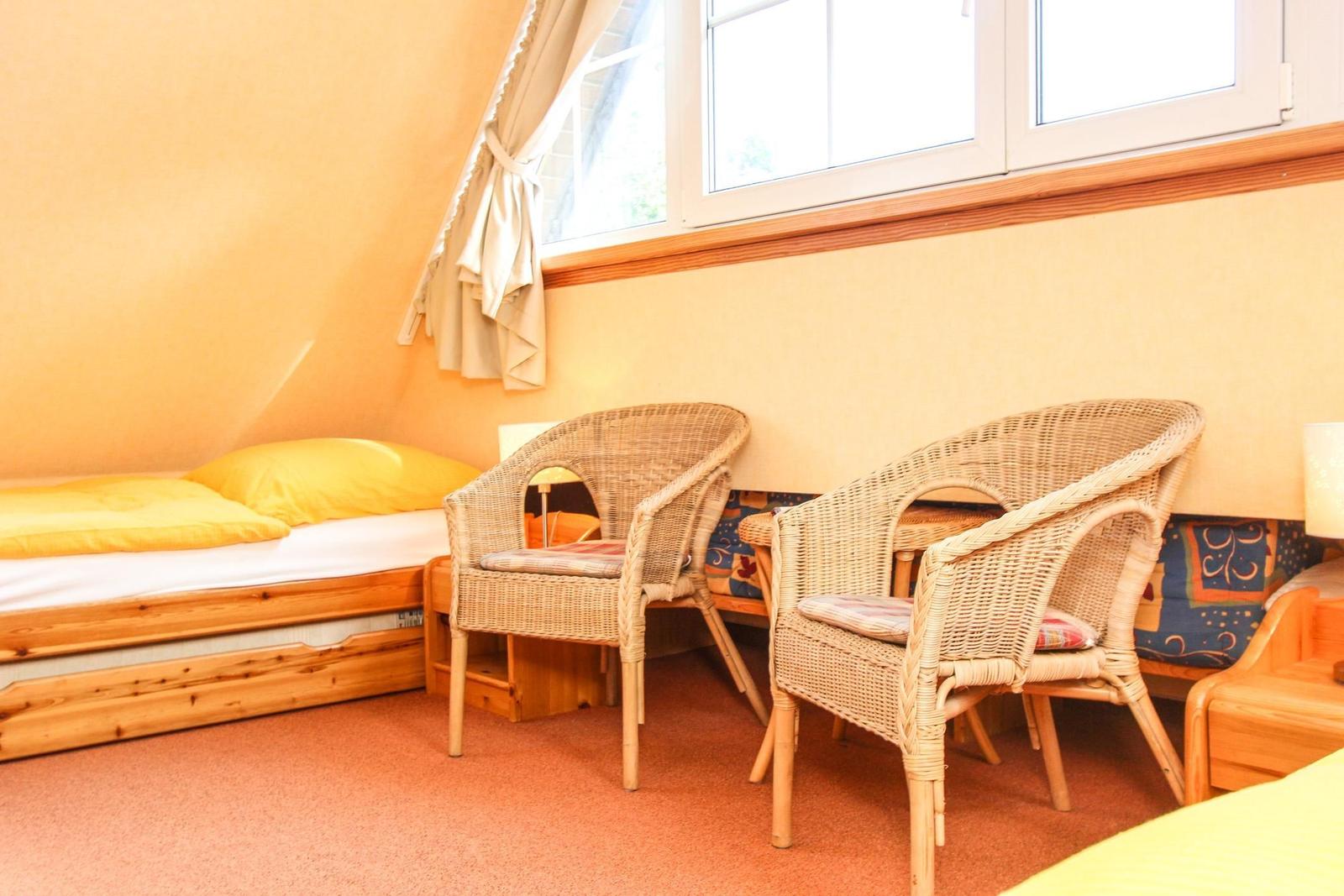 Zimmer mit Bett, zwei Stühlen und Fenster.