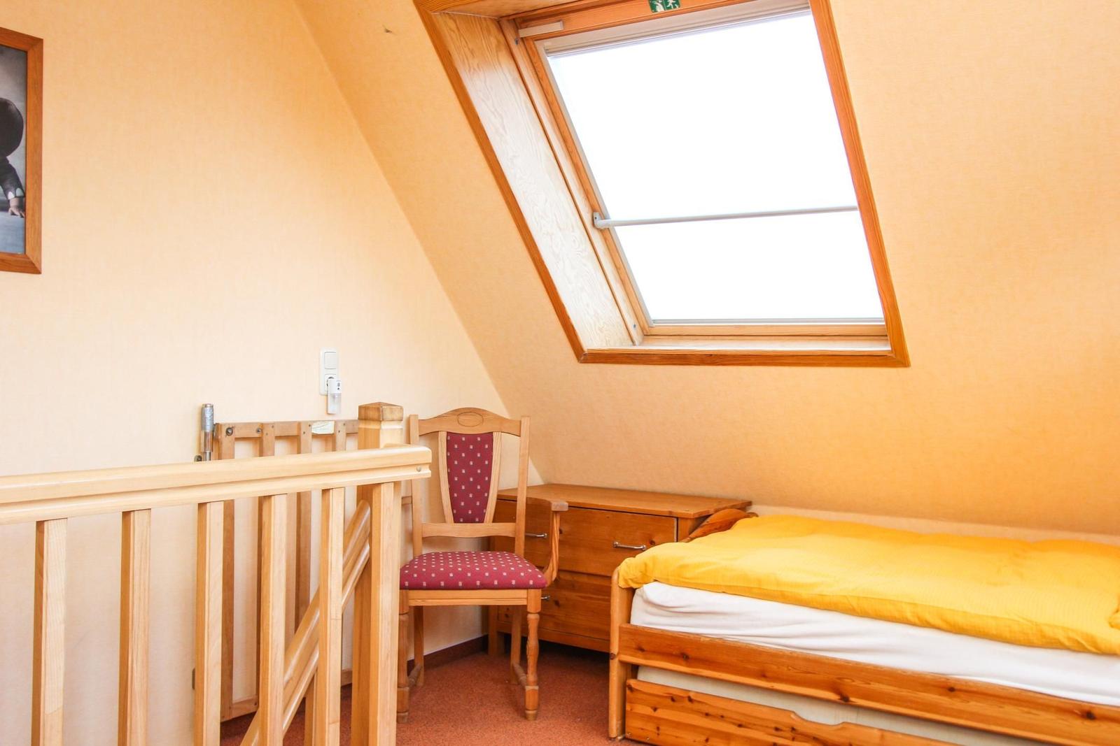 Zimmer mit Dachschrägen, Dachfenster, Bett, Stuhl und Schrank.