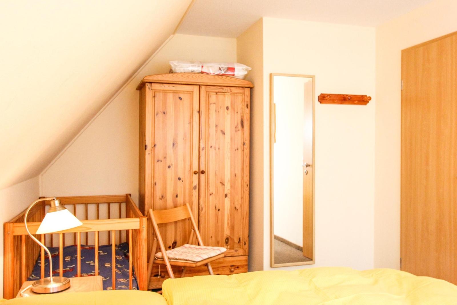 Schlafzimmer mit Holzschrank, Kinderbett und Spiegel an der Wand.