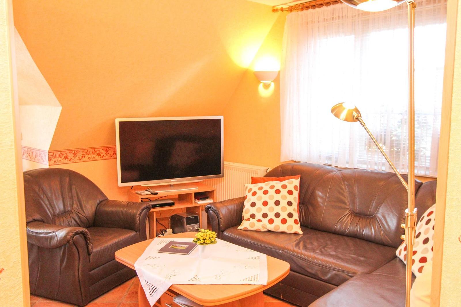Wohnzimmer mit Sofa, Sessel, Fernseher und Tisch.