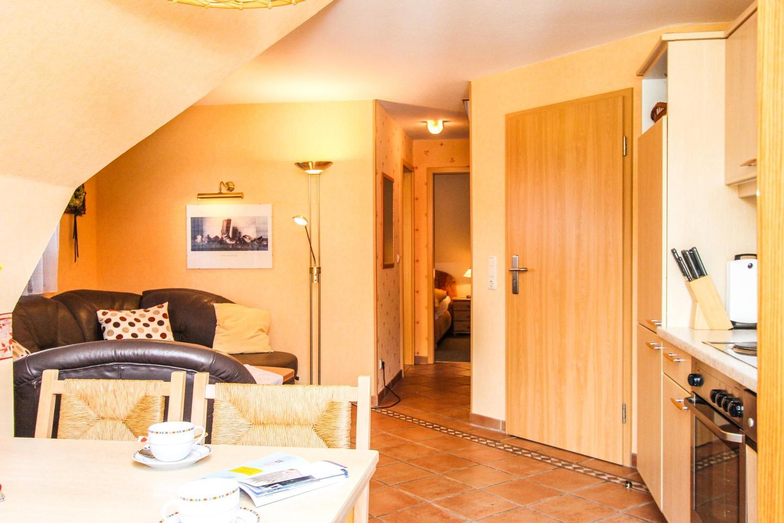 Wohnbereich mit Sofa, Esstisch und Küche. Tür führt in Schlafzimmer.