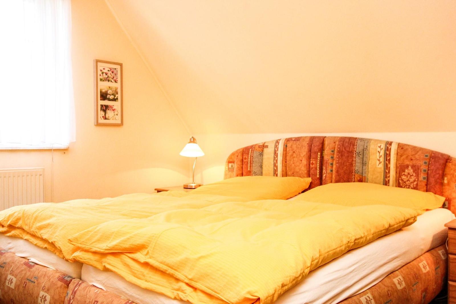 Schlafzimmer mit Bett, Nachttisch und Lampe unter schrägem Dach.