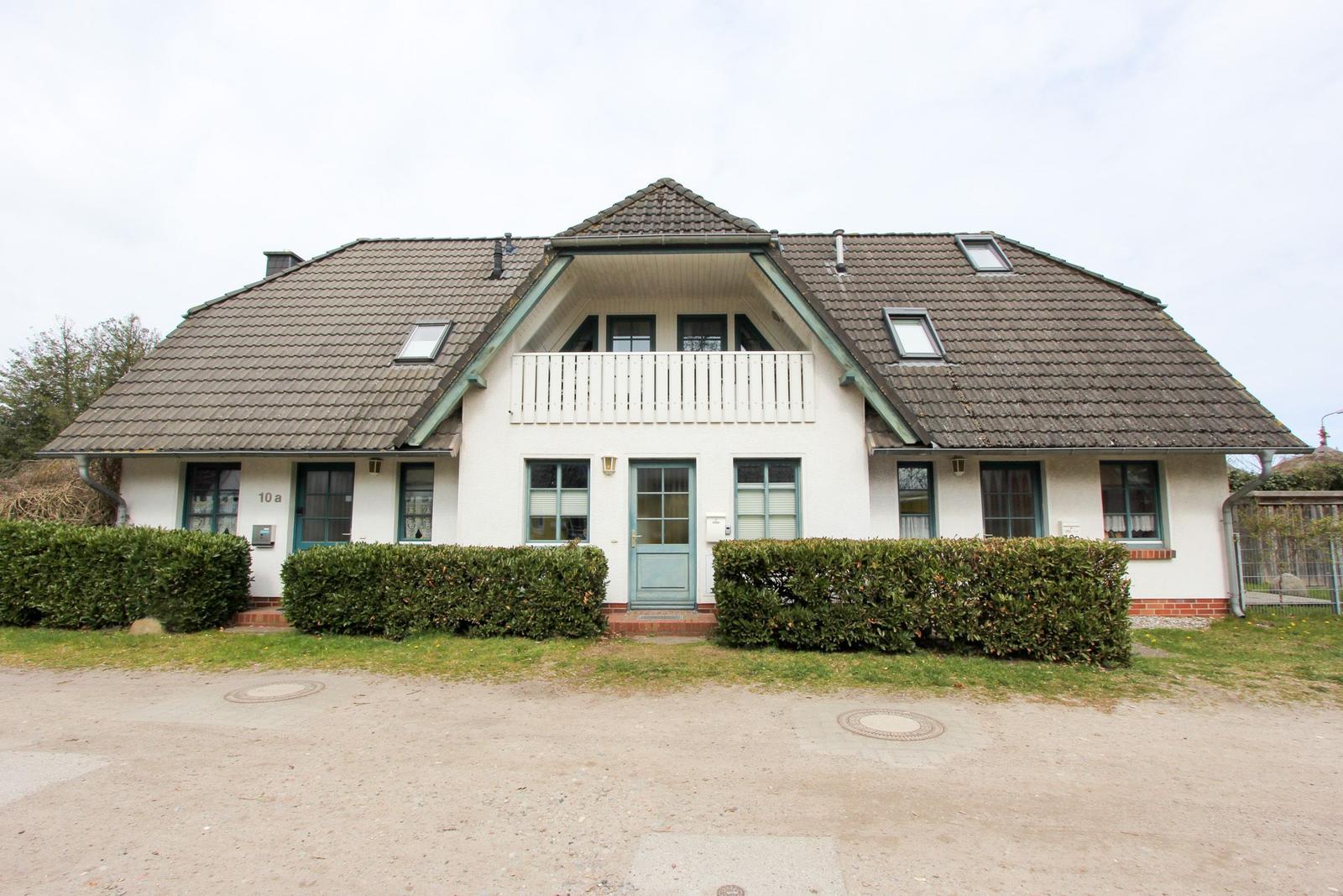 Ein zweistöckiges Haus mit Balkon, grünen Fensterrahmen und Schiebetüren.