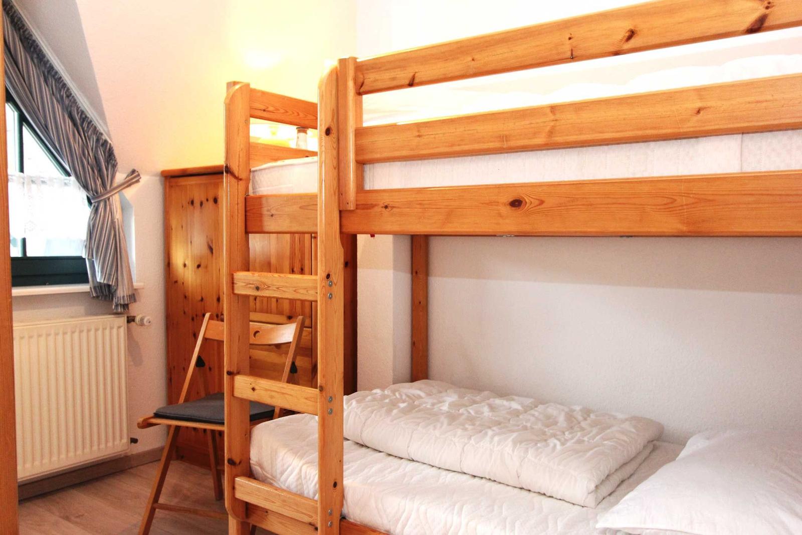 Ein Raum mit einem Holz-Etagenbett, einem Stuhl und einem Fenster mit Vorhang.