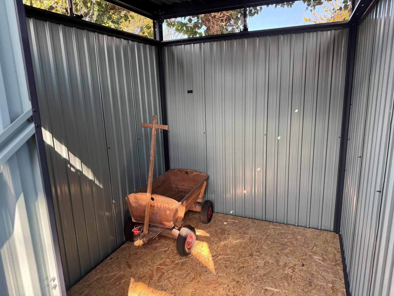 Holzschubkarre mit roten Rädern in einem Metallcontainer mit OSB-Boden.