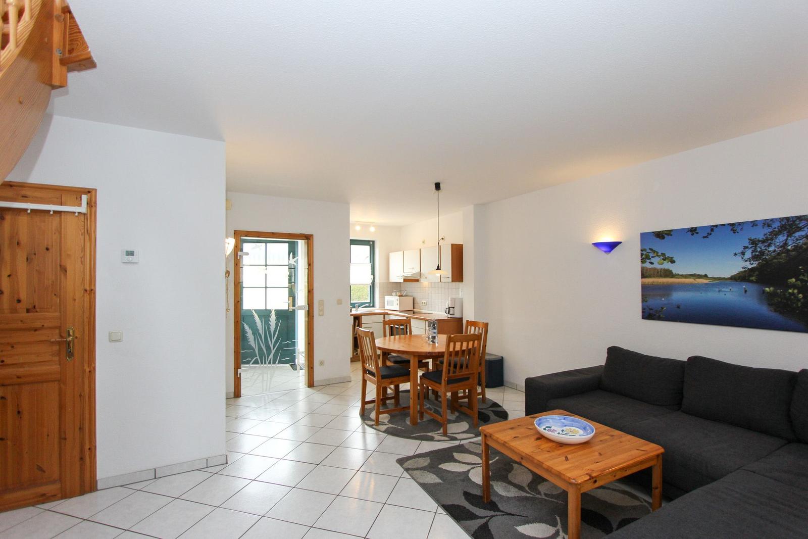 Wohnbereich mit Sofa, Esstisch und Küchenbereich. Holztür und Wandbild sichtbar.