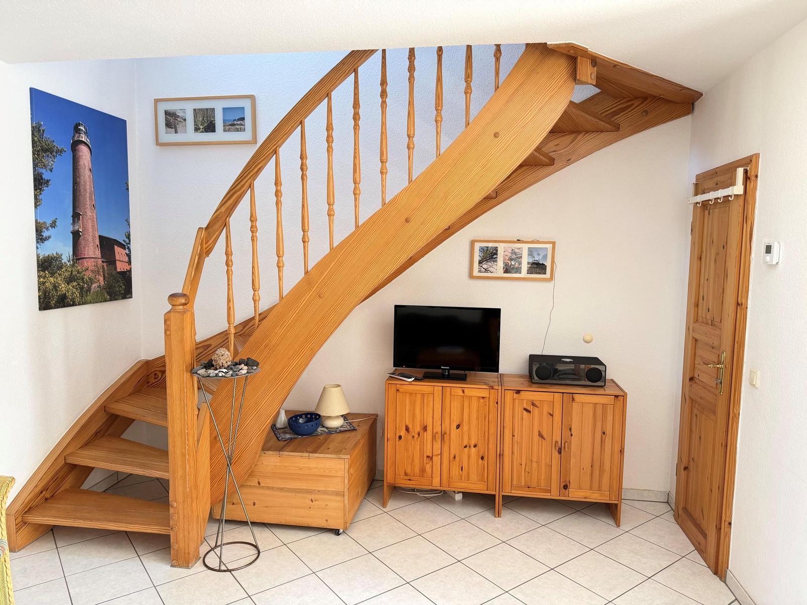 Holztreppe führt zur oberen Etage. Fernseher und Kabinett stehen im Raum.