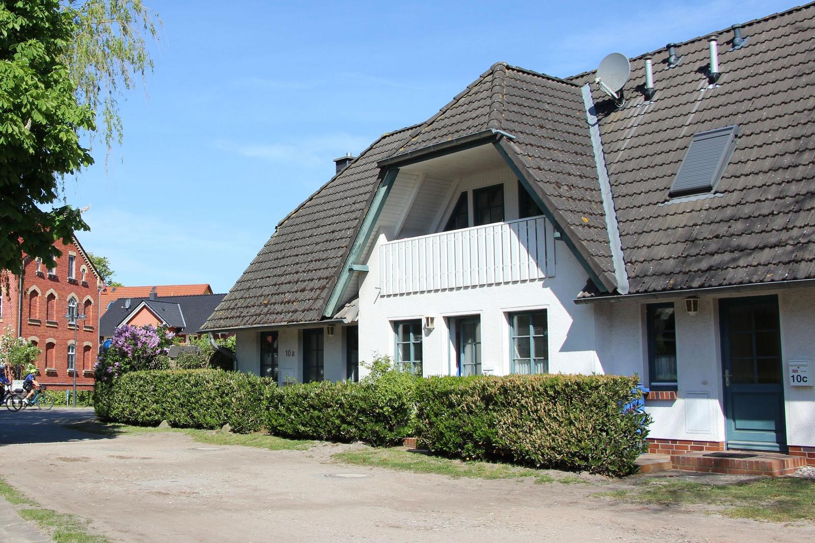 Wohnhaus mit Balkon, Dachterrasse und grüner Hecke an sonnigem Tag.