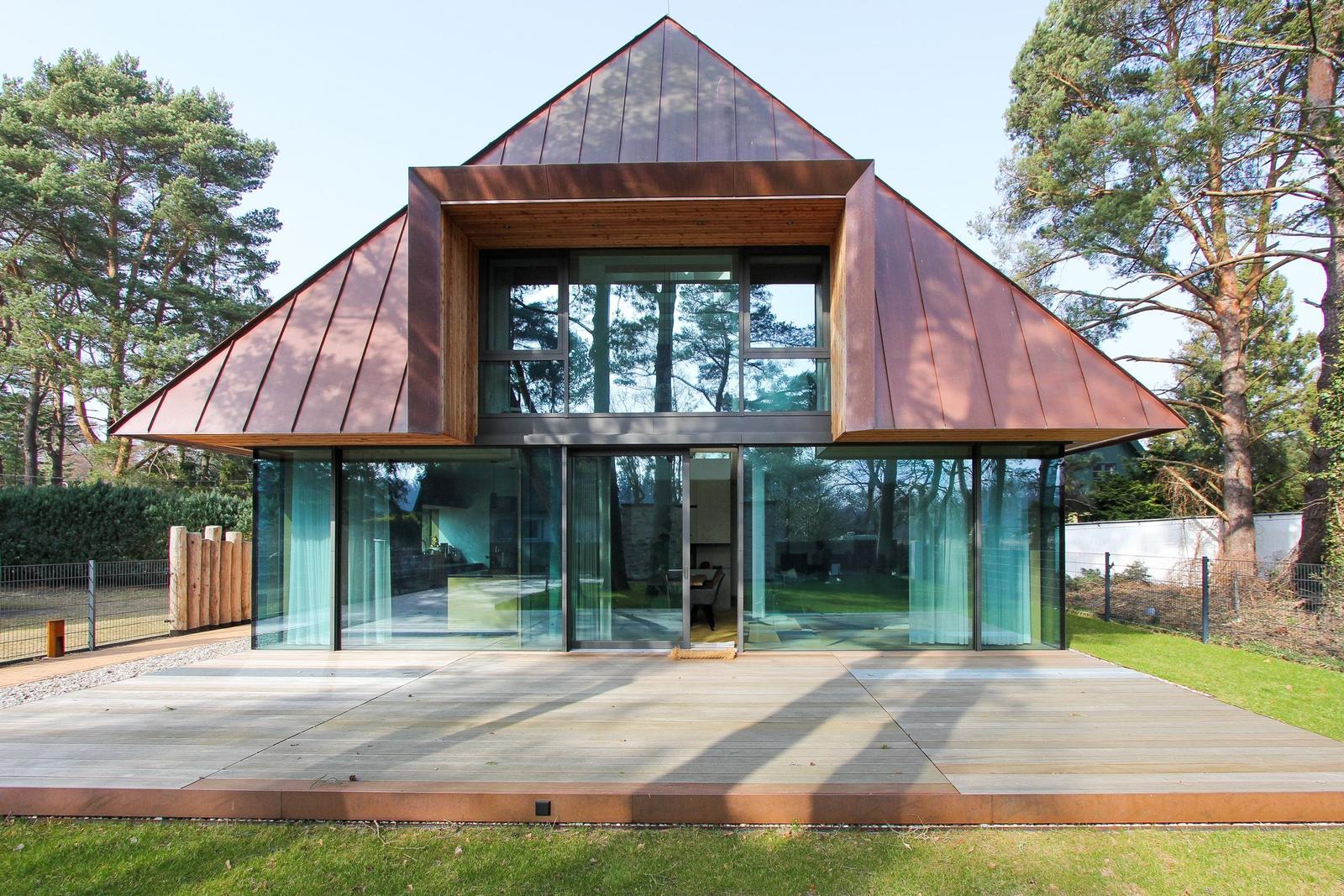 Moderne Villa mit Glasfassade und Holzverkleidung, umgeben von Bäumen und Grünfläche.
