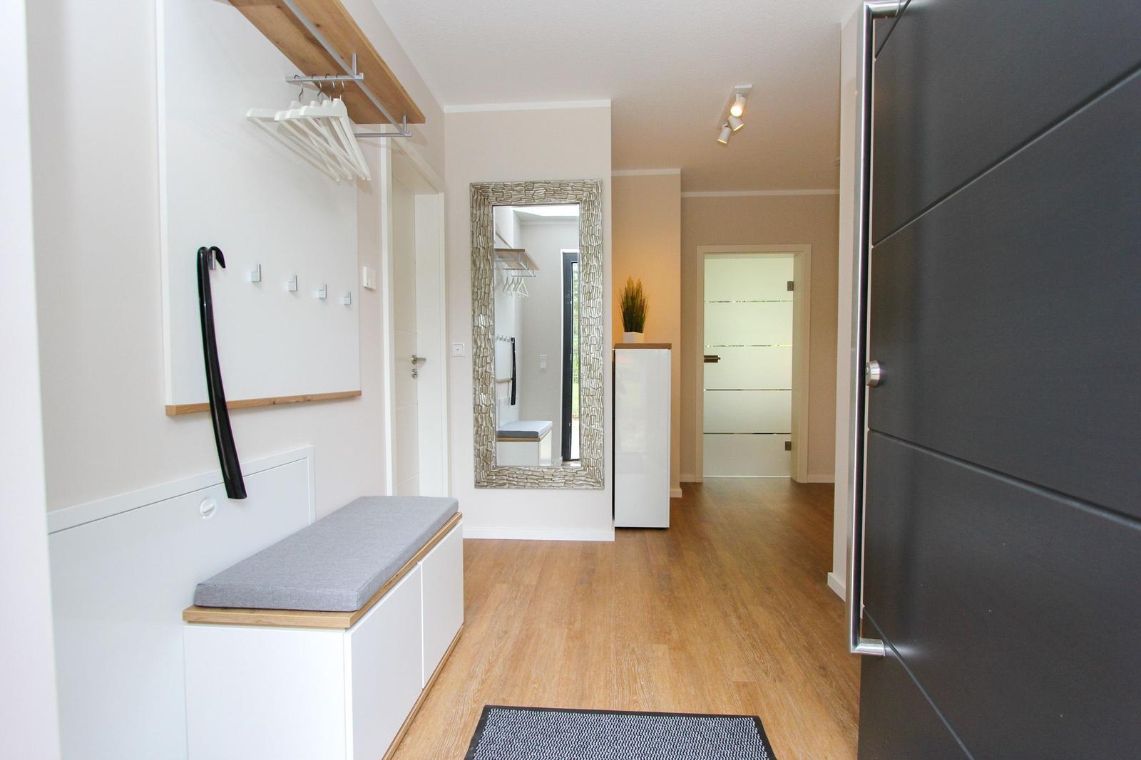 Eingangsbereich mit Garderobe, Sitzbank und Spiegel. Holzboden und moderne Einrichtung.