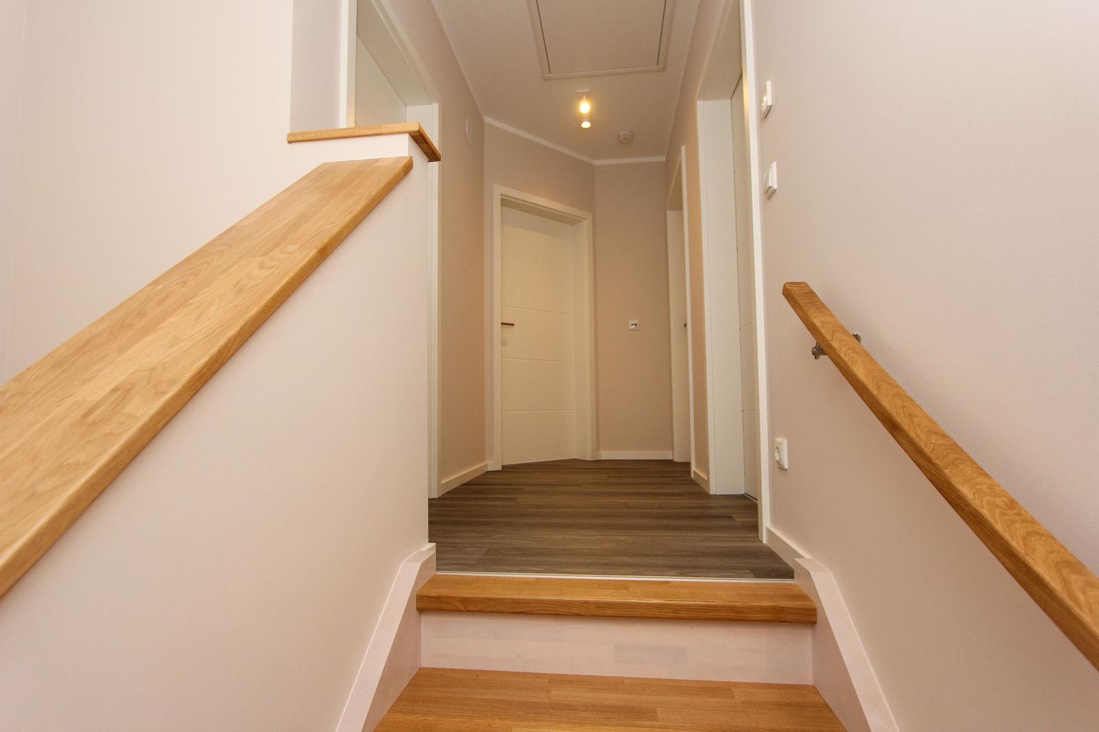 Hausflur mit Holzgeländer und Treppenstufen, Boden aus Holz, weiße Wände und Decke.