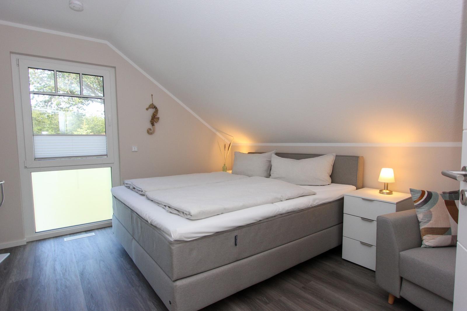 Schlafzimmer mit Doppelbett, Nachttisch und Sessel. Fenster mit Blick auf Außenbereich.