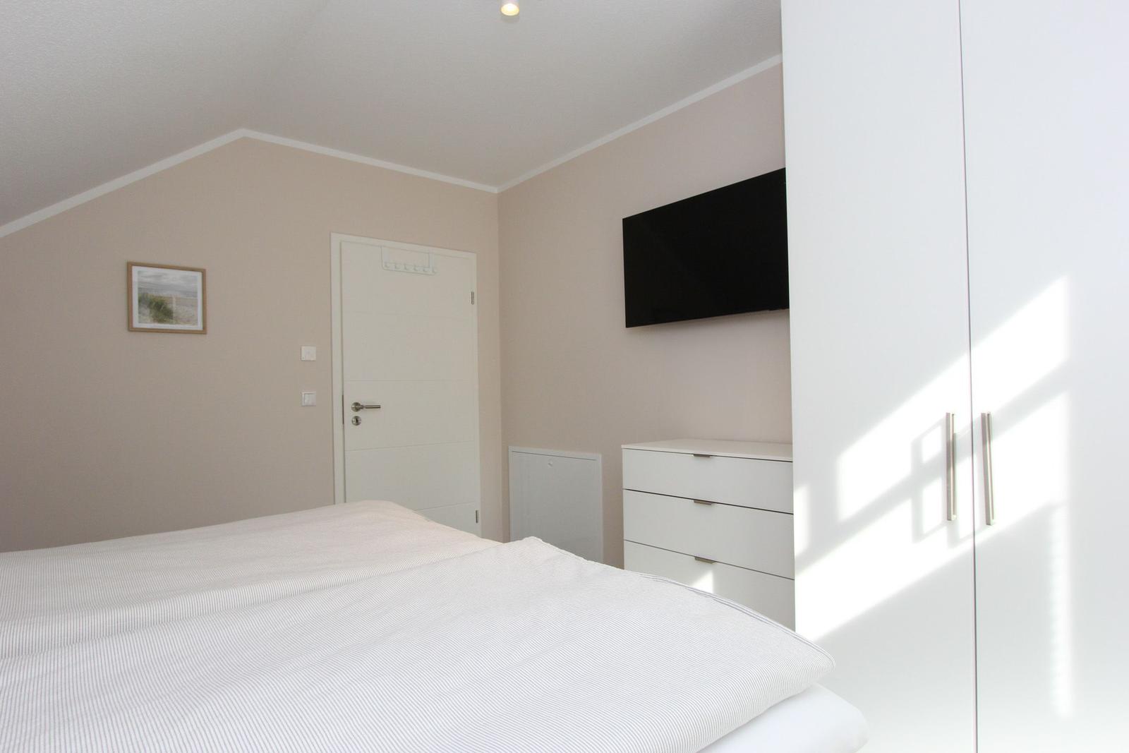 Schlafzimmer mit Bett, Kleiderschrank und Fernseher an der Wand.
