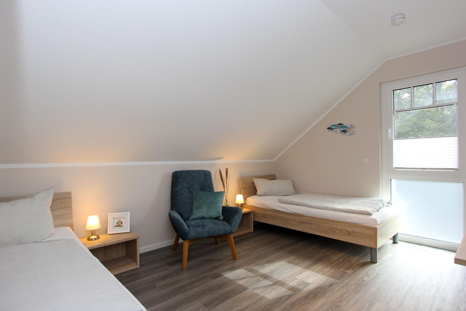 Zimmer mit zwei Betten, Stuhl und Fenster. Holzboden und schräges Dach.