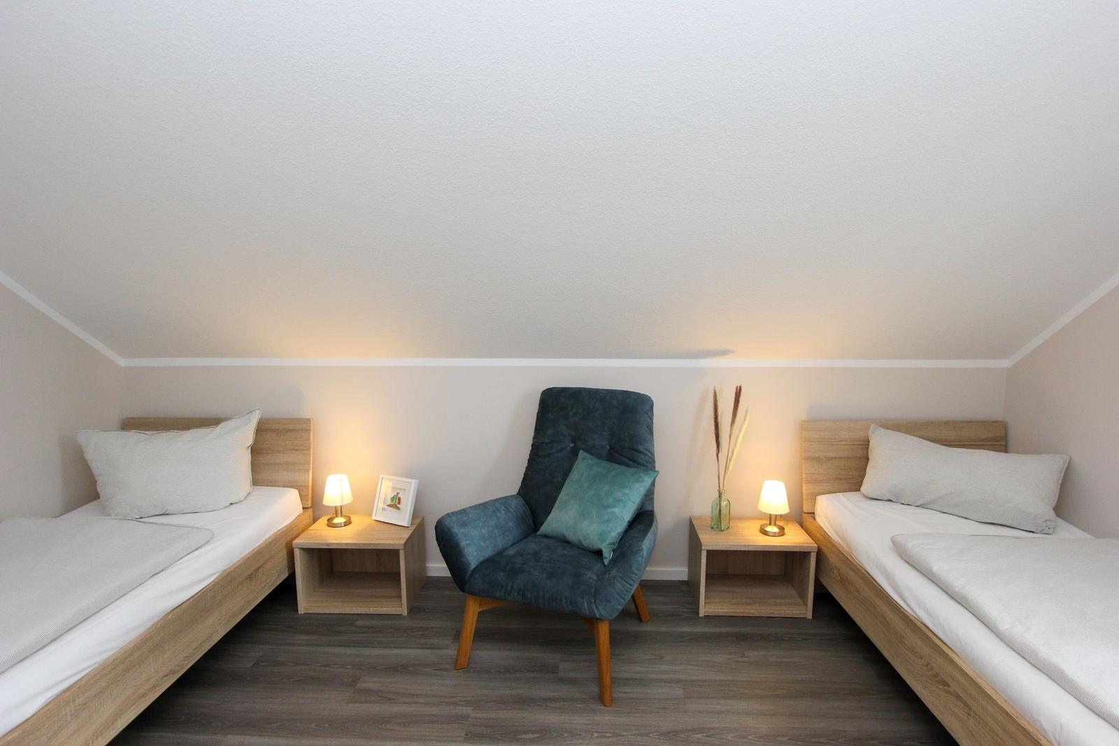 Zwei Einzelbetten und ein Sessel mit Beistelltischen und Lampen.