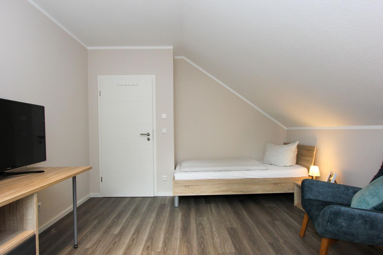 Zimmer mit Bett, Fernseher und Sessel unter Dachschrägen