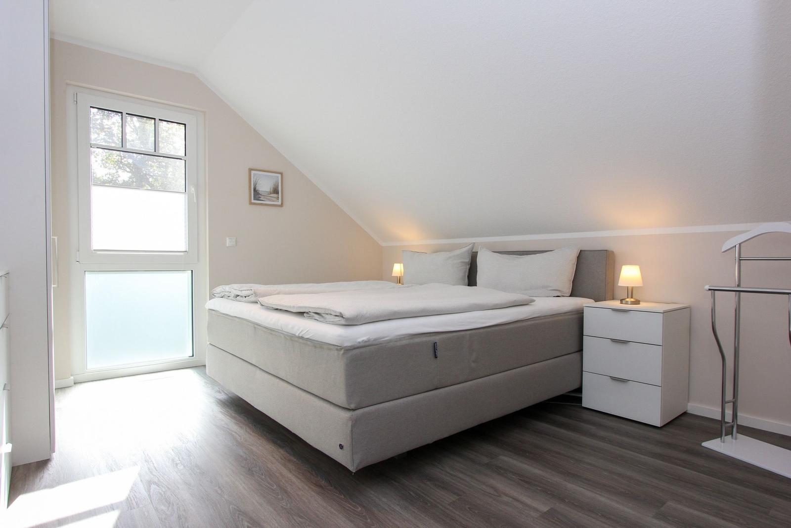Schlafzimmer mit Doppelbett, Nachttisch und Fenster. Holzfußboden und schräge Decke.