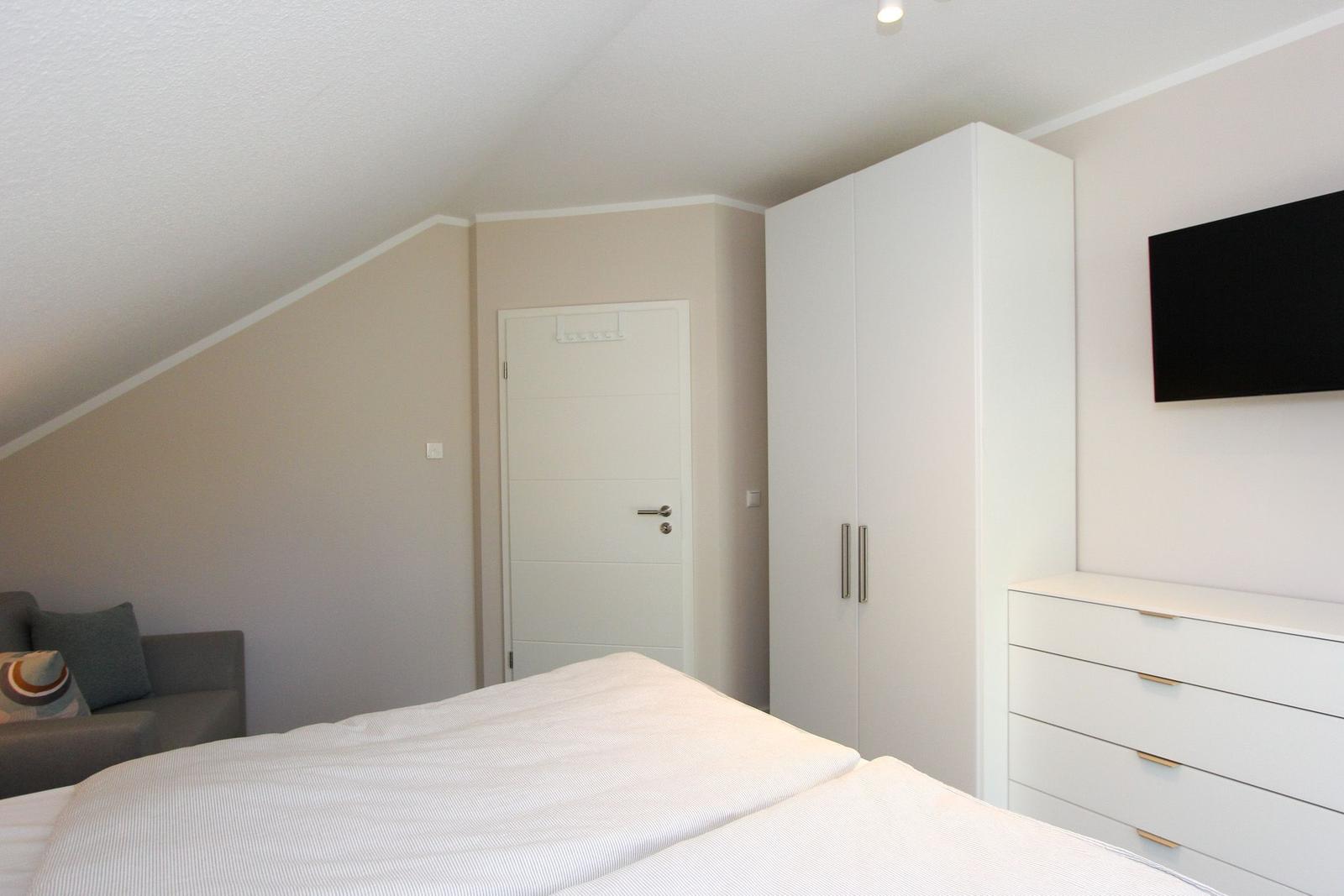 Schlafzimmer mit Dachschrägen, Bett, Kleiderschrank und Fernseher an der Wand.