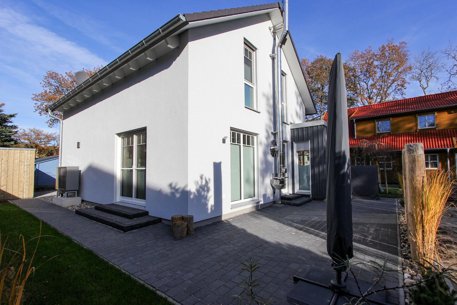Moderne weiße Villa mit Terrasse und Garten. Schwarze Dachrinne und Fenster sind sichtbar.