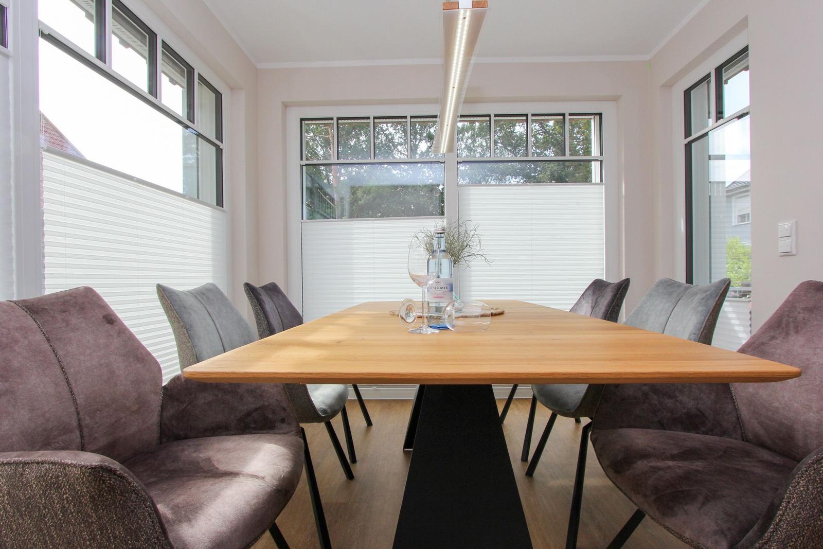 Esszimmer mit Holztisch und Stühlen, großen Fenstern und moderner Beleuchtung.