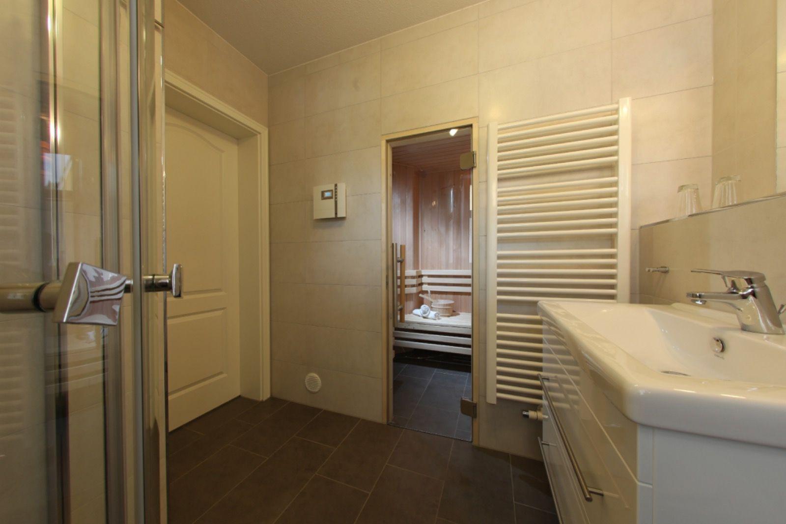 Badezimmer mit Dusche, Waschbecken und Sauna im Hintergrund.
