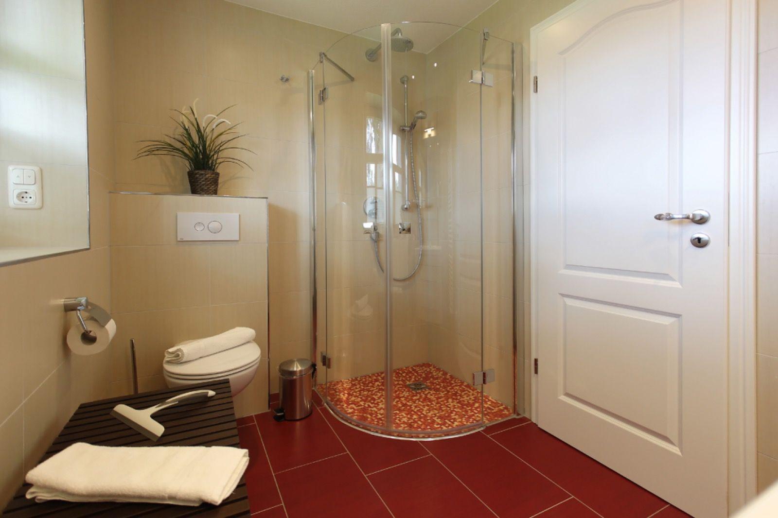 Badezimmer mit Dusche, Toilette und Badewanne. Bodenfliesen rot, Wandfliesen beige.