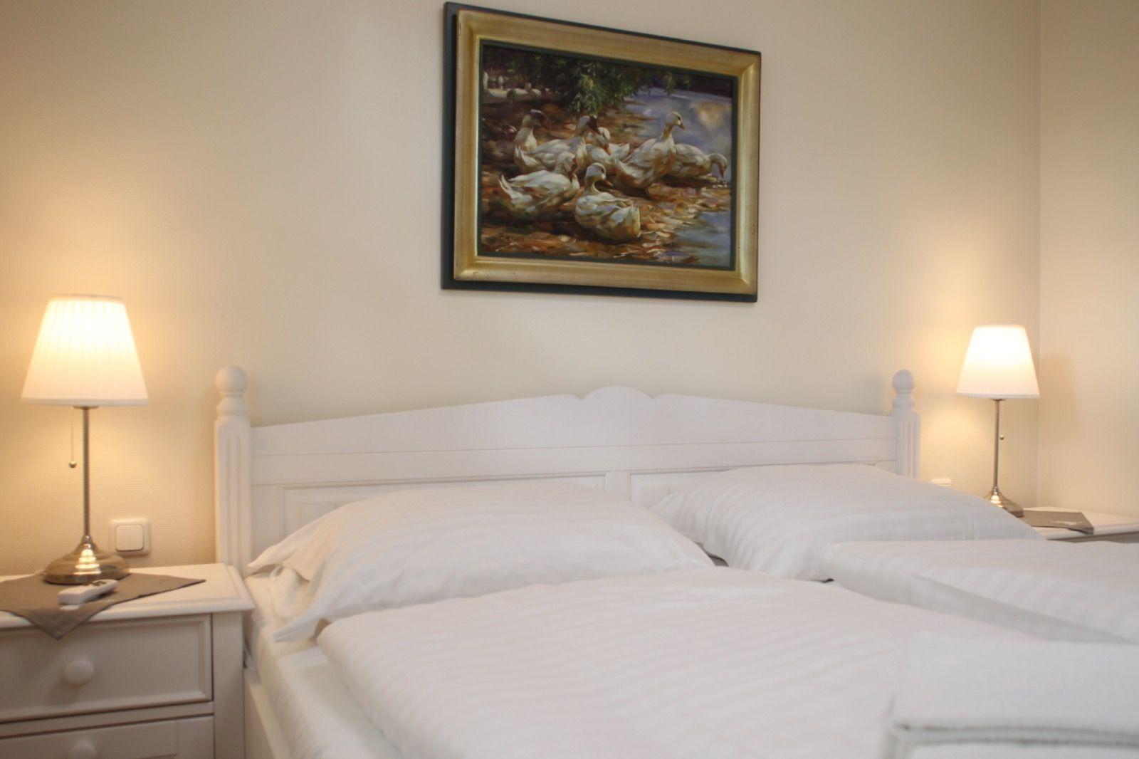 Schlafzimmer mit weißem Bett, Nachttisch und Wandbild mit Enten.