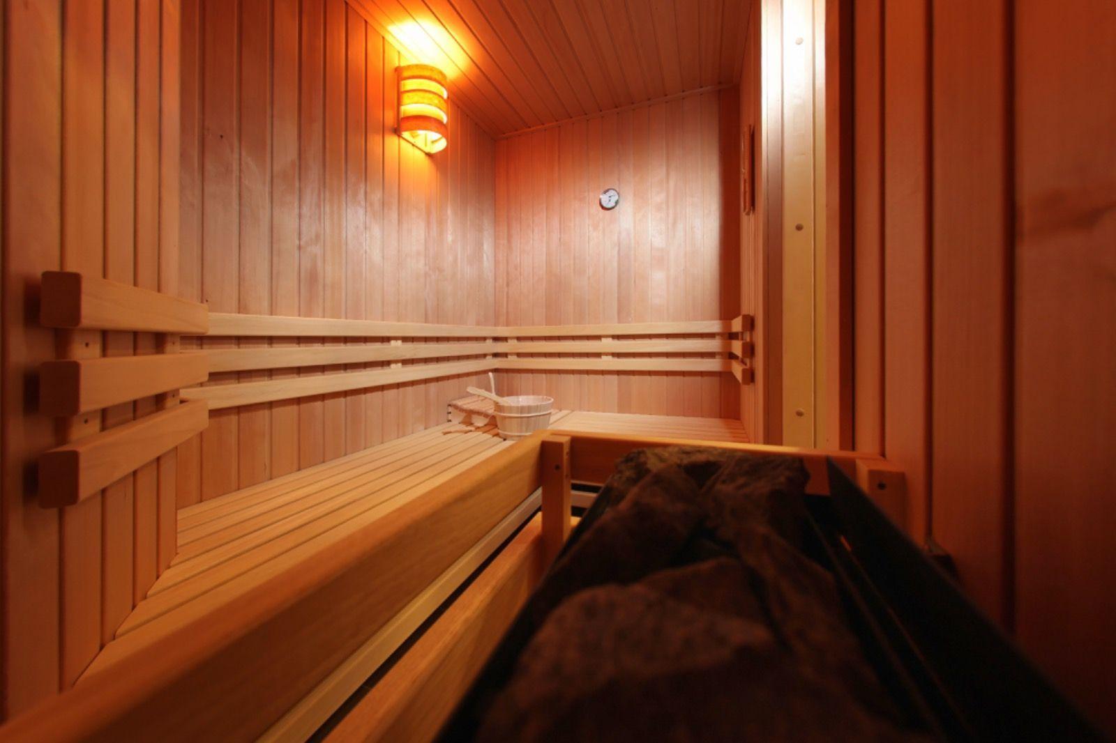 Sauna mit Holzbank, Wärmegeber und Thermometer an der Wand.