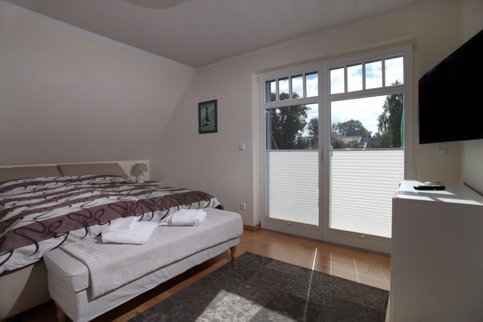 Schlafzimmer mit Doppelbett, TV und Balkontür mit Blick auf Grünflächen.