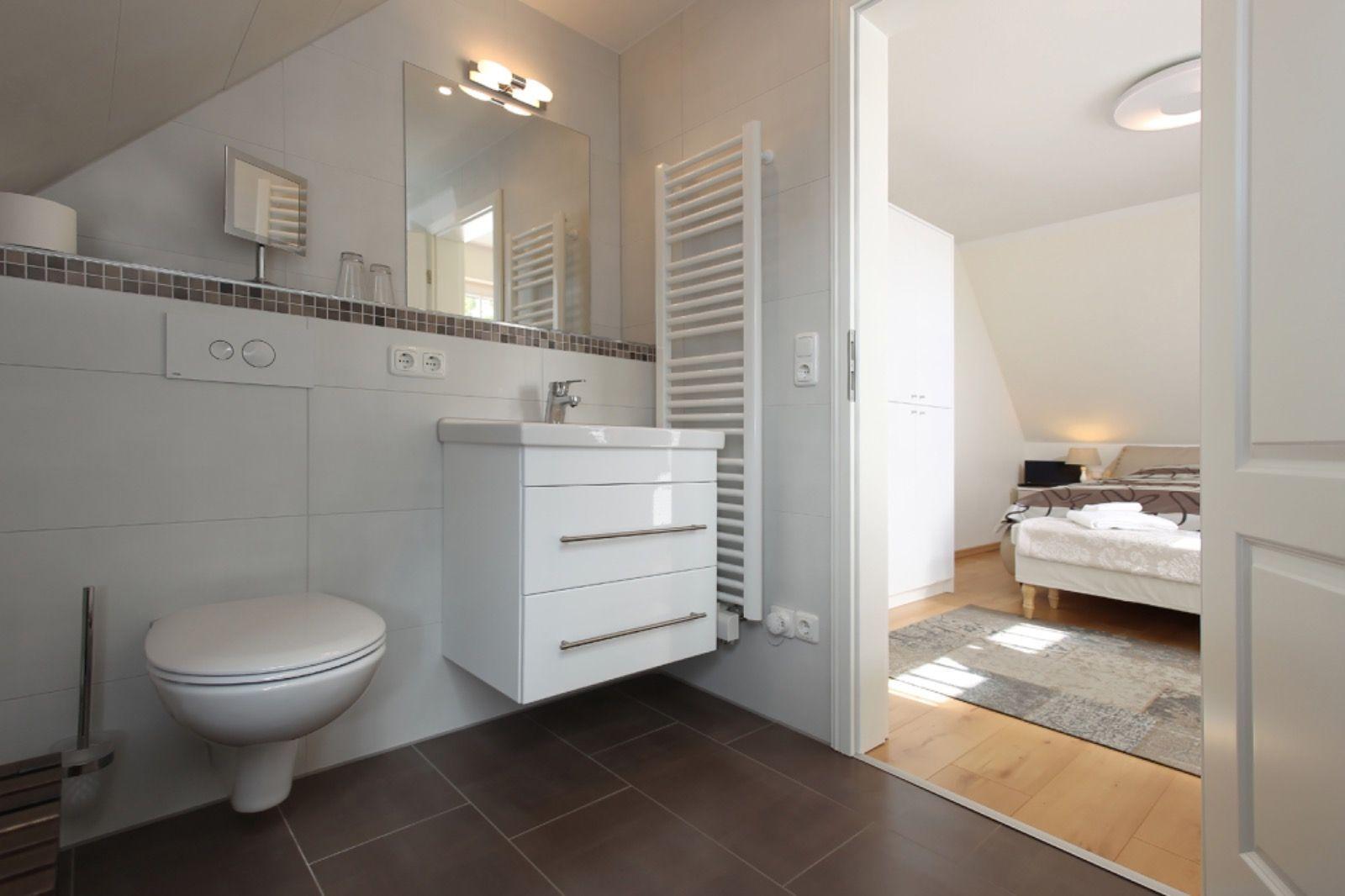 Badezimmer mit Toilette, Waschbecken und Heizkörper. Durchgang zur Schlafzimmer.