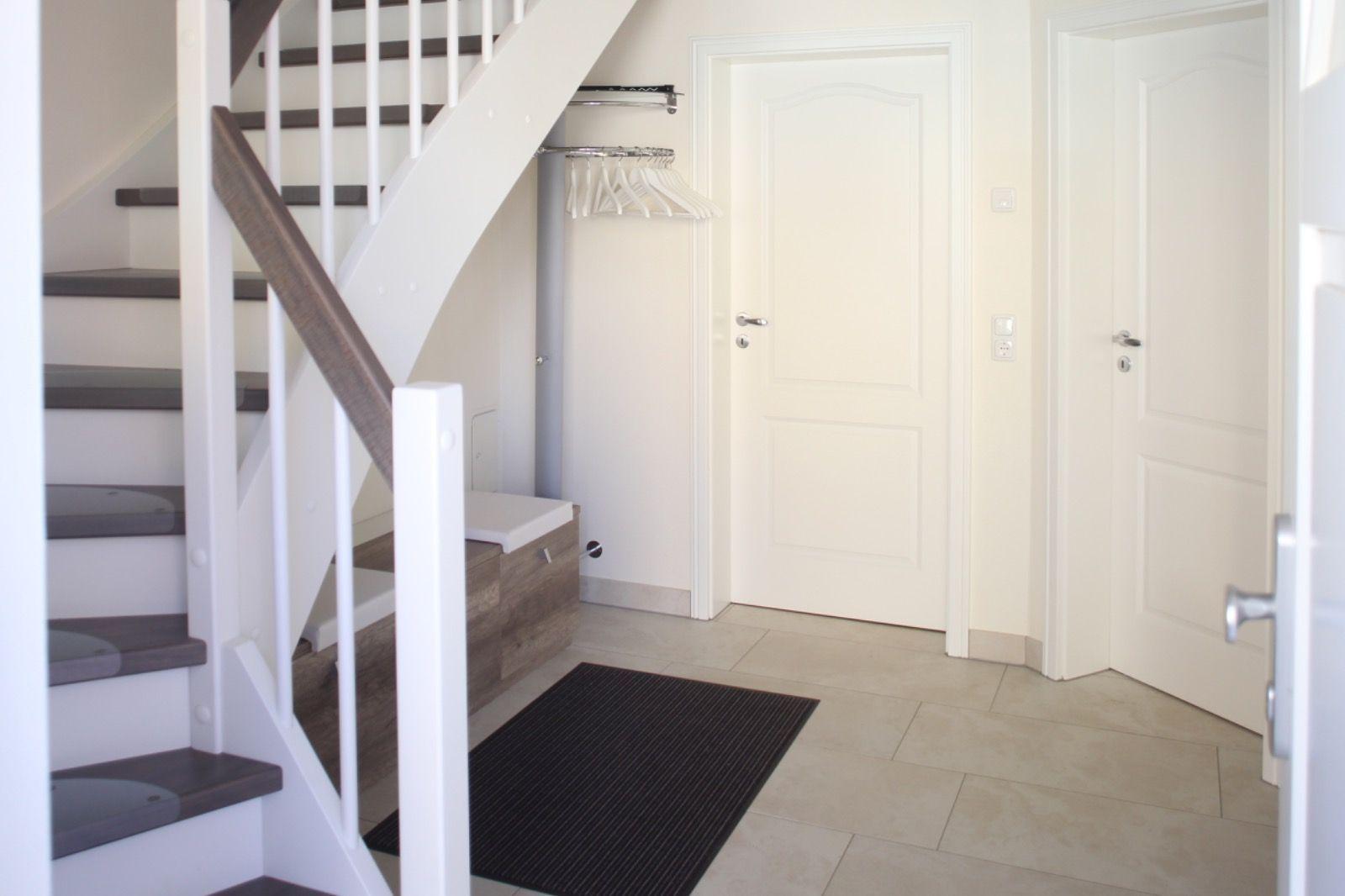 Hausflur mit Treppe, Kleiderständer und zwei Türen.