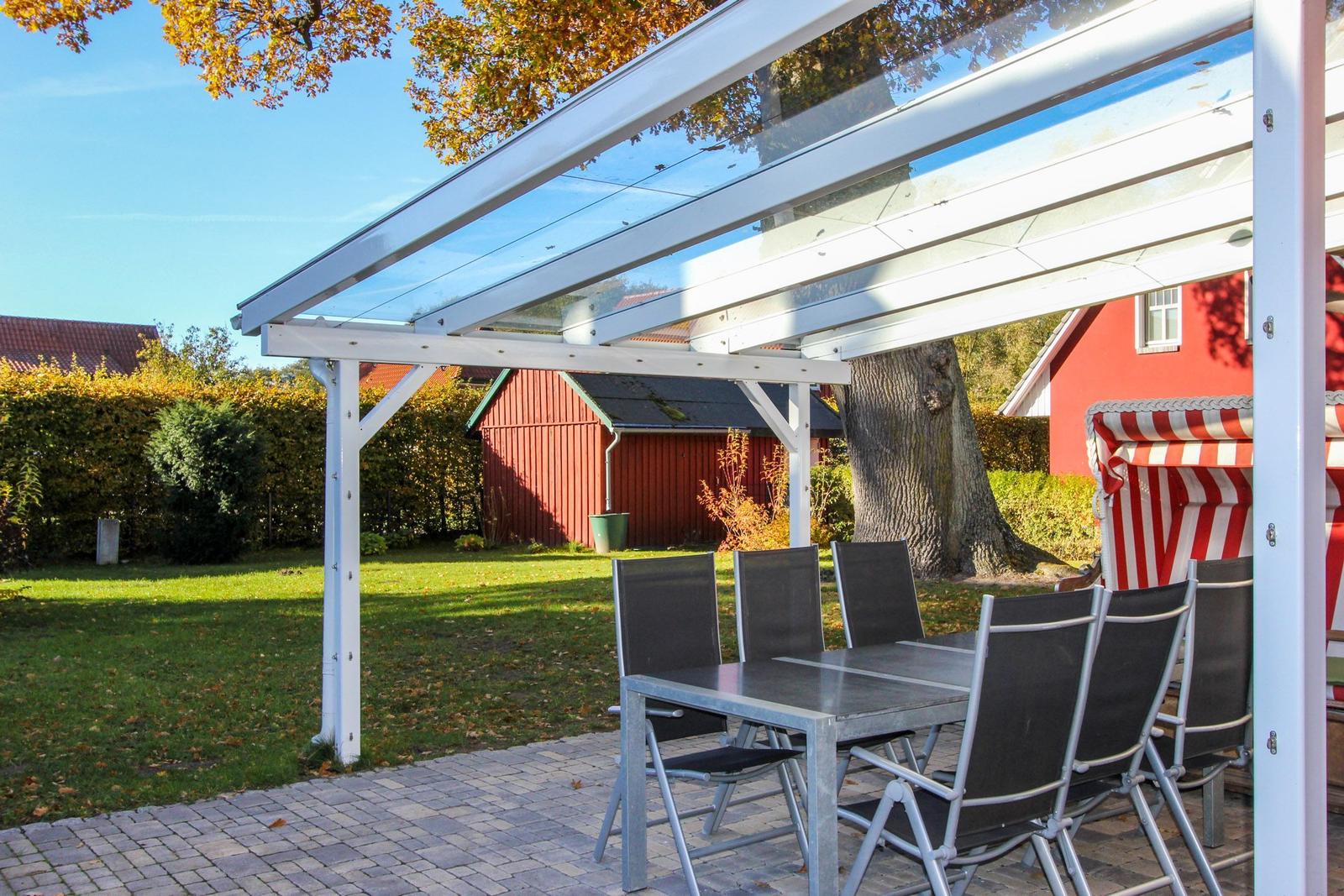Terrasse mit Glasdach, Tisch und Stühlen. Hintergrund: rote Scheune und Baum.