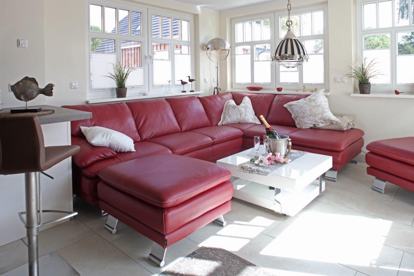 Ein Wohnzimmer mit rotem Ledersofa, weißem Couchtisch und großen Fenstern.