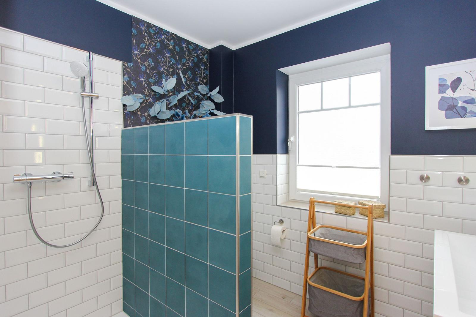 Bad mit Dusche, Fenster und Holzregal. Wände mit blauen und weißen Fliesen.